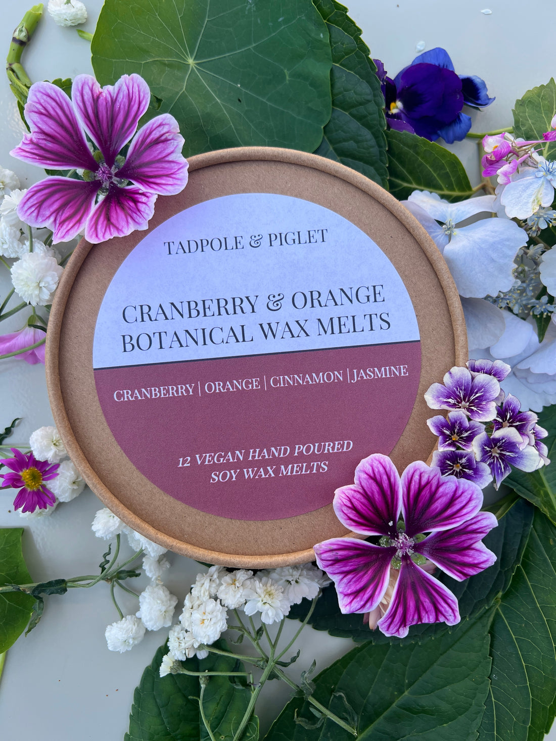 Cranberry and Orange Botanical Wax Melts in round container with flowers and green leaves