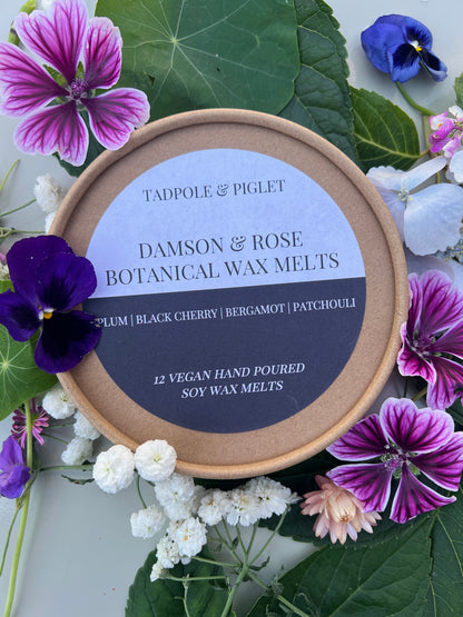 Damson &amp; Rose Botanical Wax Melts packaging surrounded by vibrant flowers, highlighting luxurious fragrance notes.