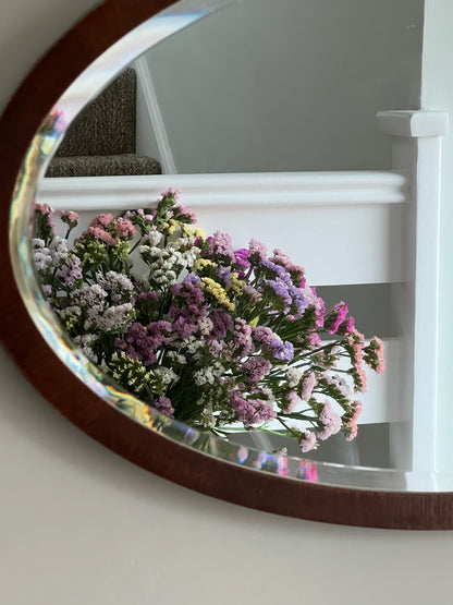 Reflection of a vibrant bouquet of mixed statice flowers in a round mirror, showcasing their rich summer colors.