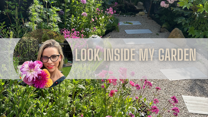 Woman holding colorful flowers in a vibrant garden with a pathway, inviting viewers to explore her garden.